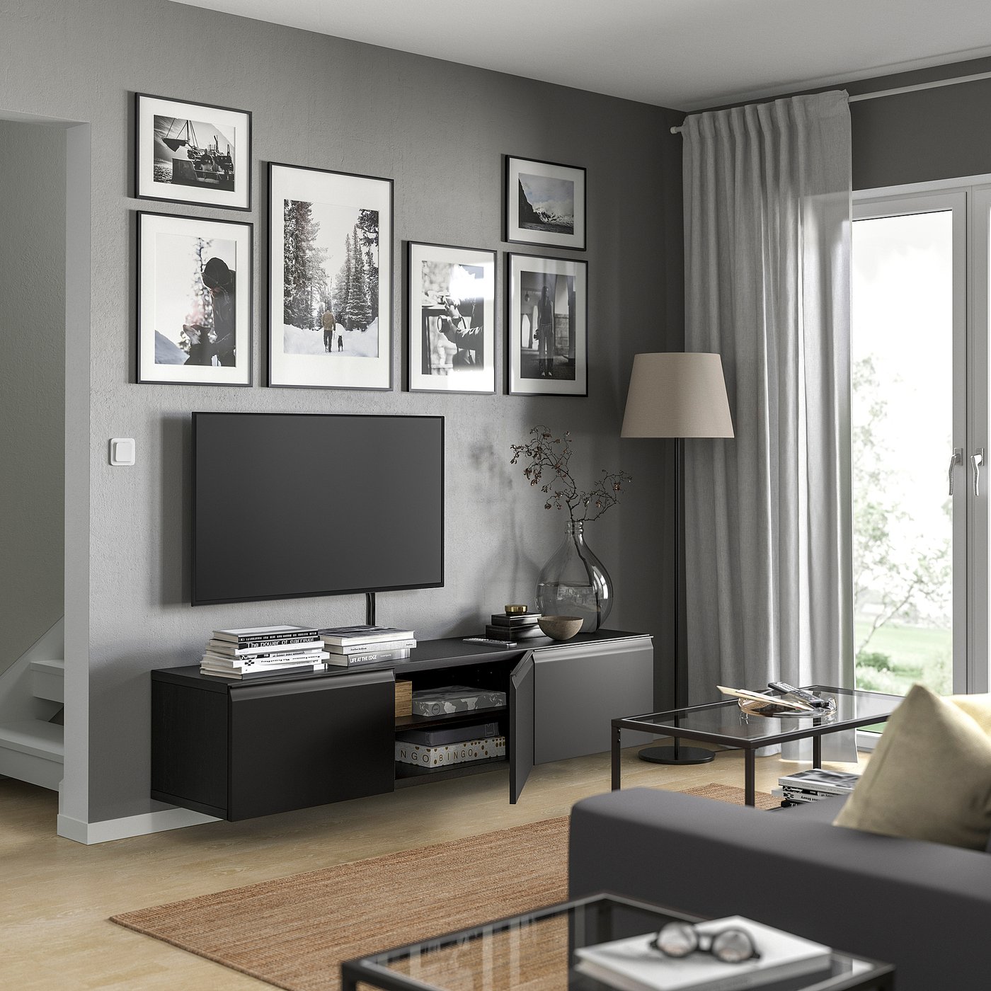 Modern living room with black BESTÅ tv bench, artwork, lamp, and cosy decor. Large window with curtains, wooden floor, and sleek furniture.