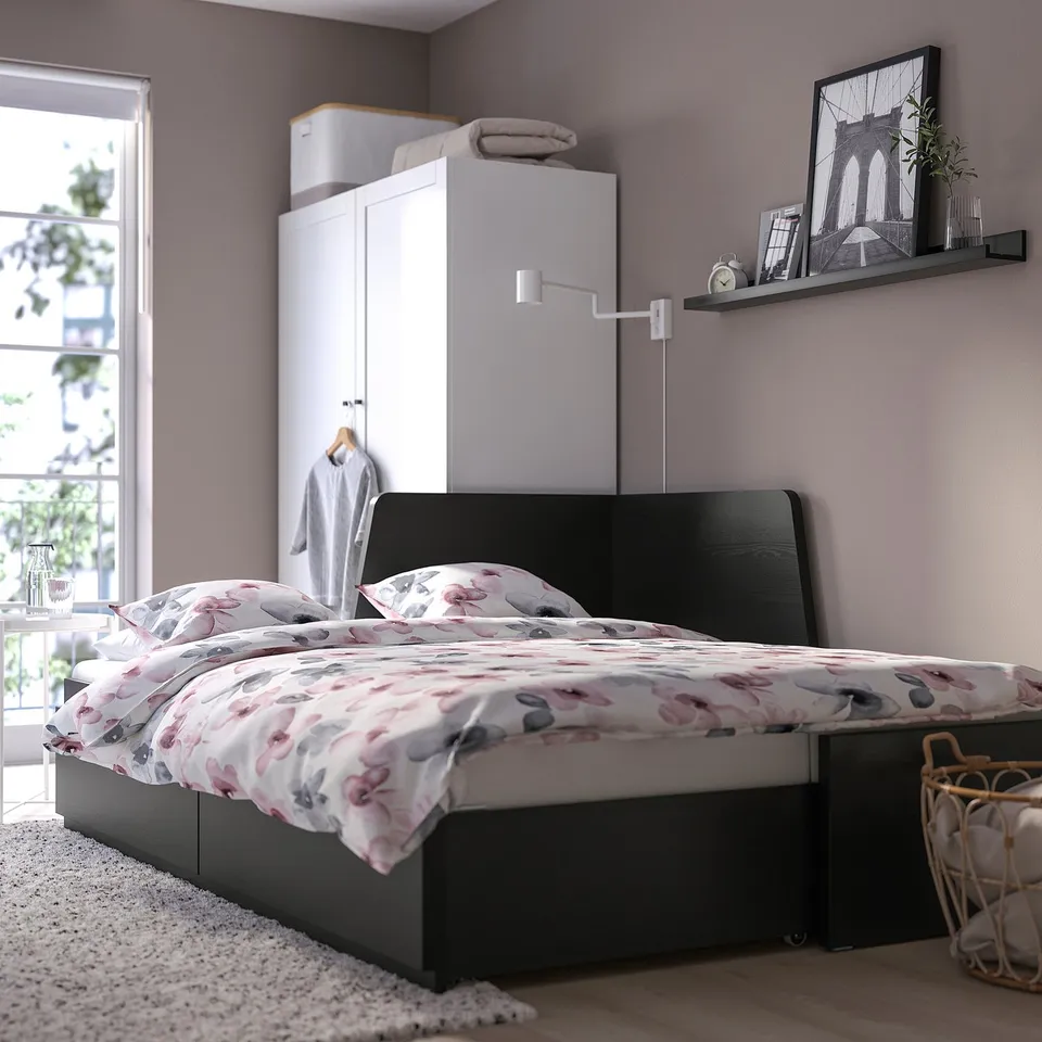 Modern bedroom with black day-bed featuring floral bedding, drawers, and wall-mounted shelf with decor.