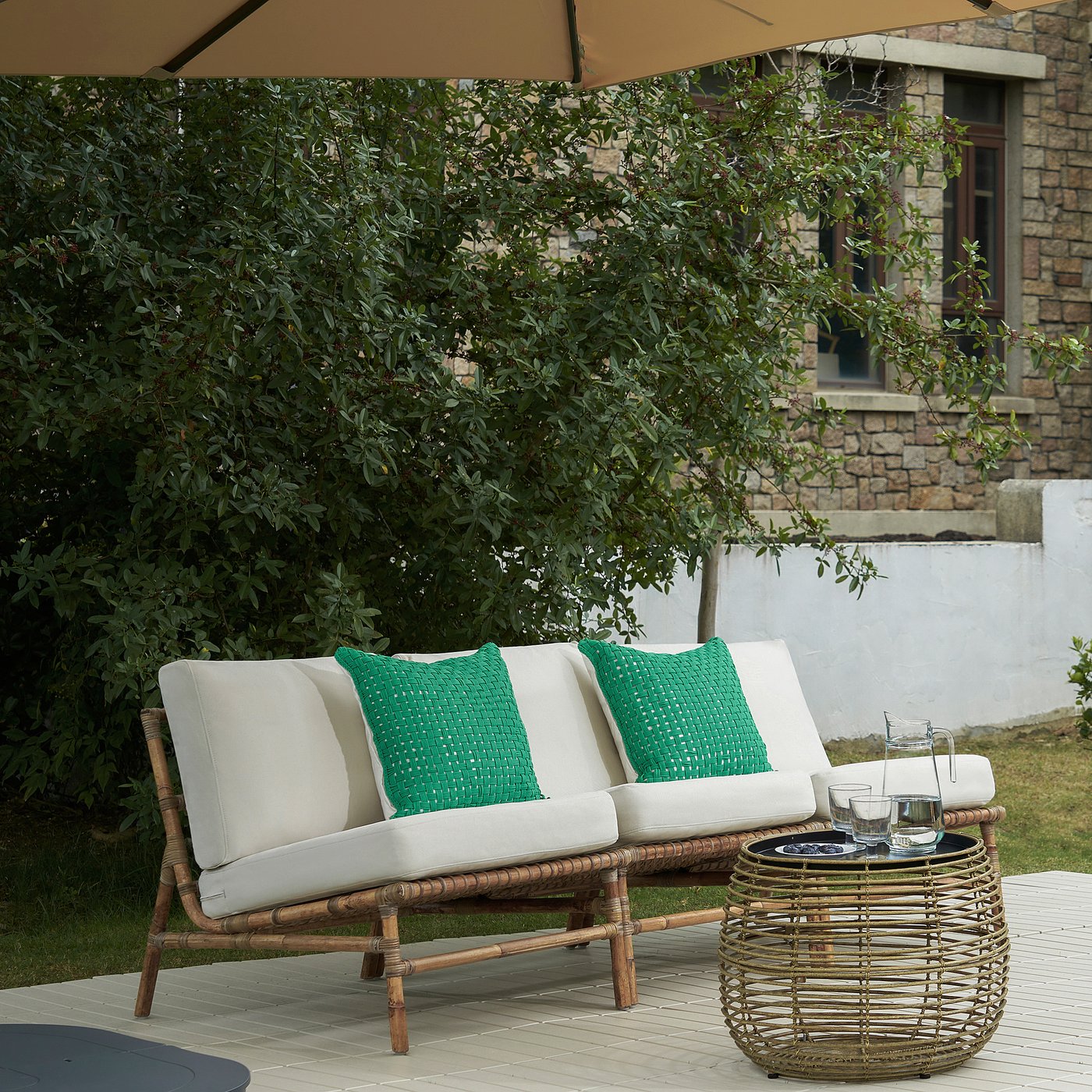 TVARÖ outdoor sofa: stylish, comfortable, natural-brown rattan with white cushions and green pillows, perfect for outdoor relaxation.