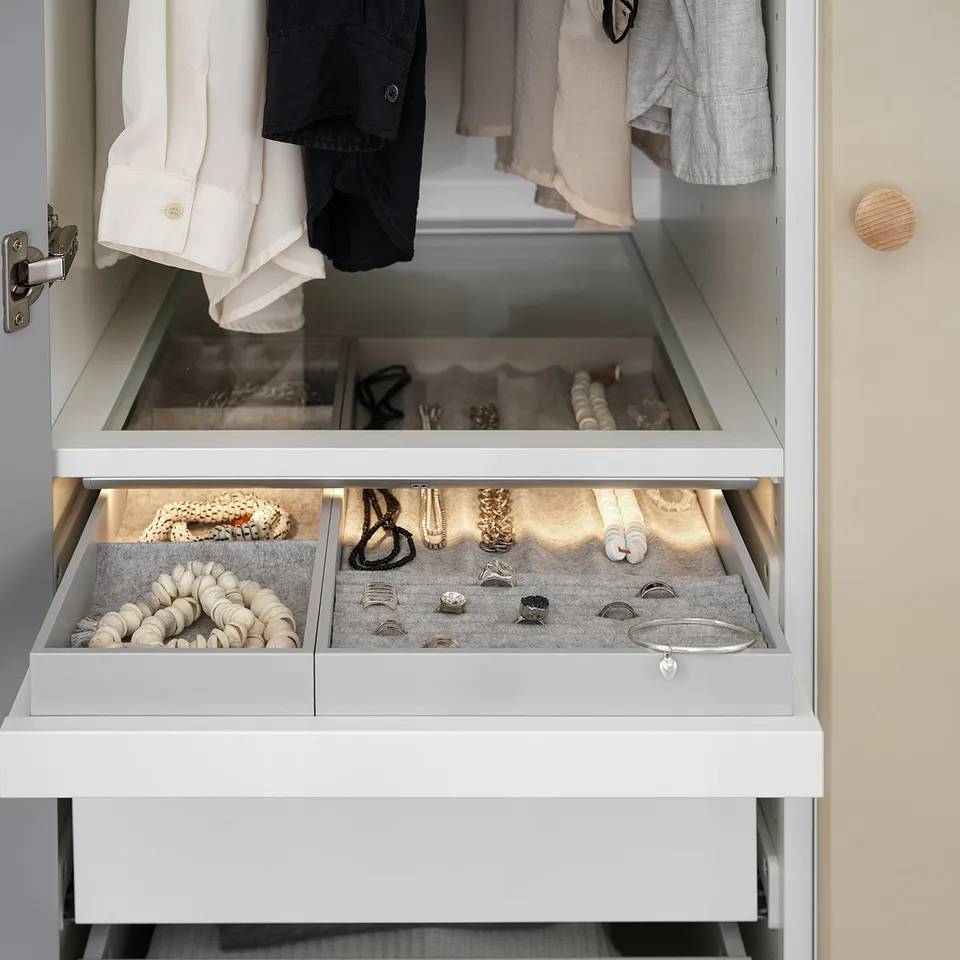 Organised closet drawer with jewellery and clothes. Two open white felt-lined compartments holding rings, bracelets, necklaces, and watches.