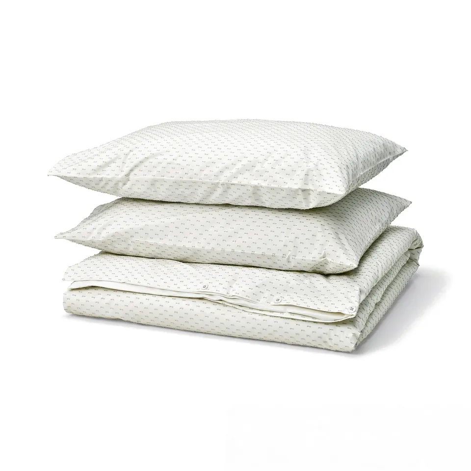 A stack of three white BANDKNIPPE cotton duvet covers with green polka dots, neatly folded.