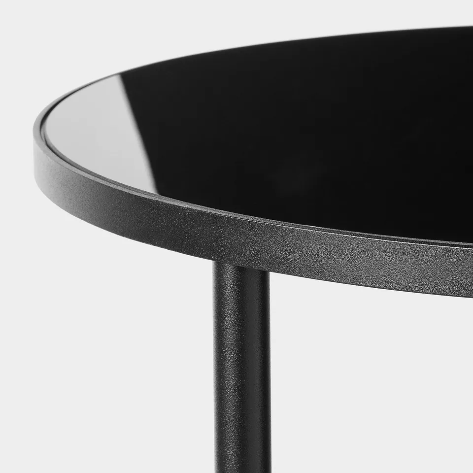 Modern round table with sleek black glass top, designed for durability and style.