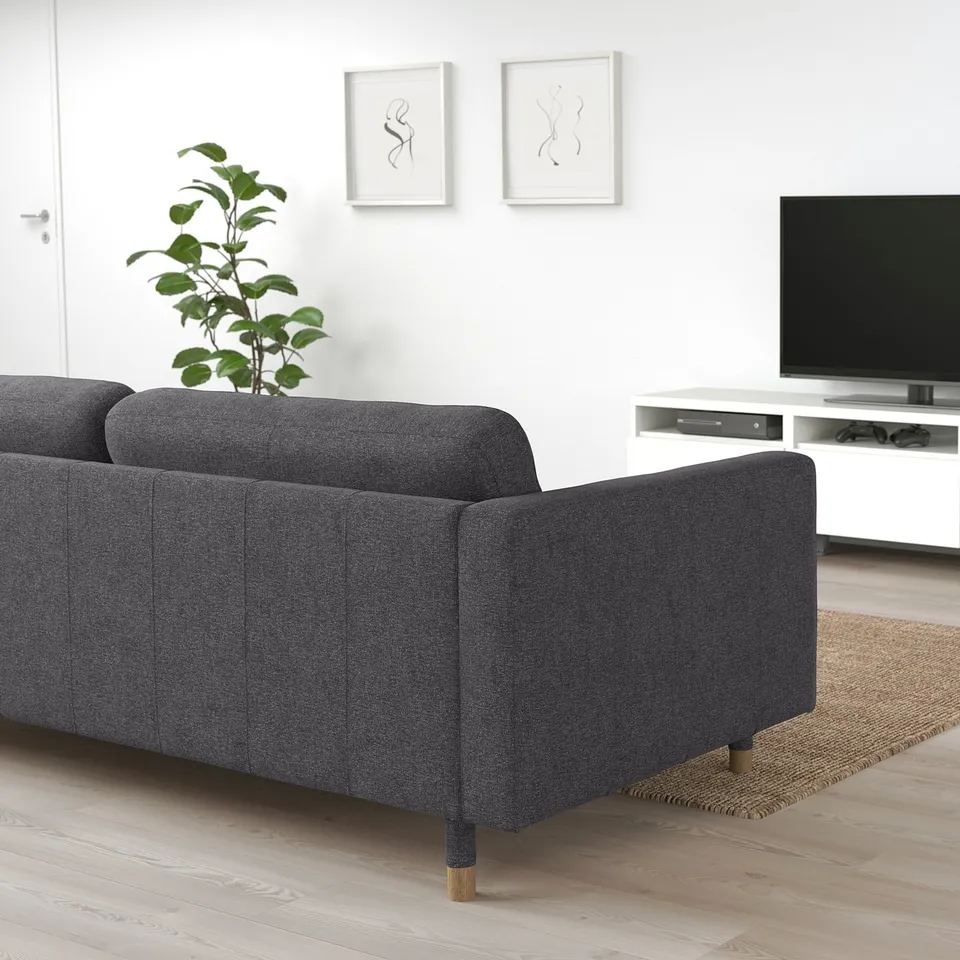 Modern minimalist living room: dark grey LANDSKRONA sofa, large tv on white stand, wall art, potted plant, rug.
