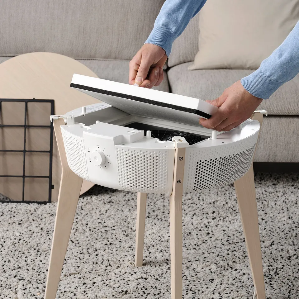 Person instals STARKVIND air philtre in living room, showing easy replacement process.