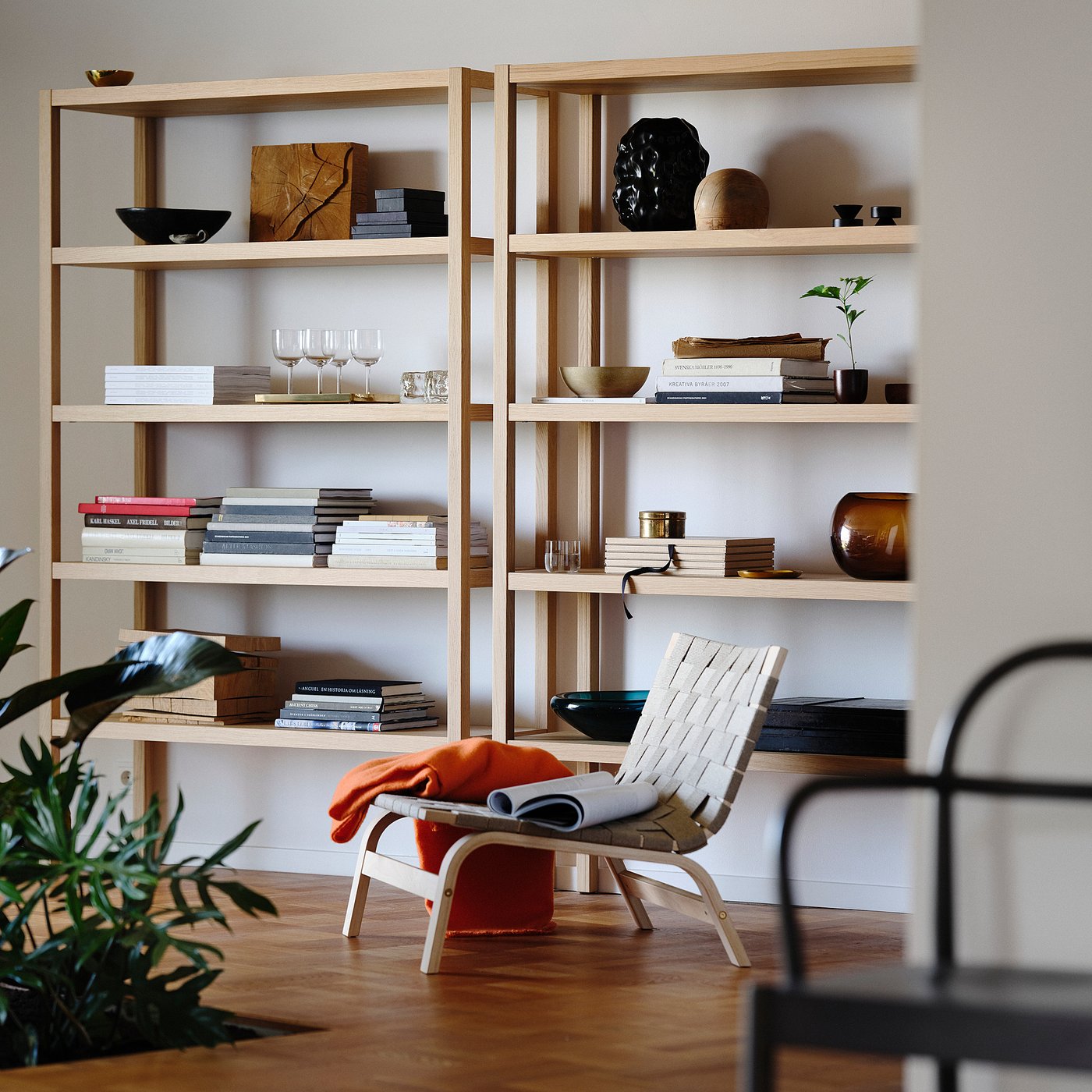Modern living room with light wood shelves, scandinavian chair, plants, books, vases, and wine glasses.