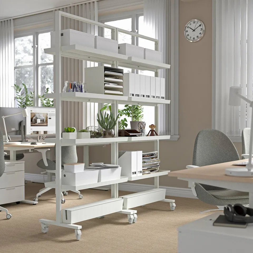 Modern office with mobile shelving unit holding books, plants, and supplies, dividing and organising workspace.
