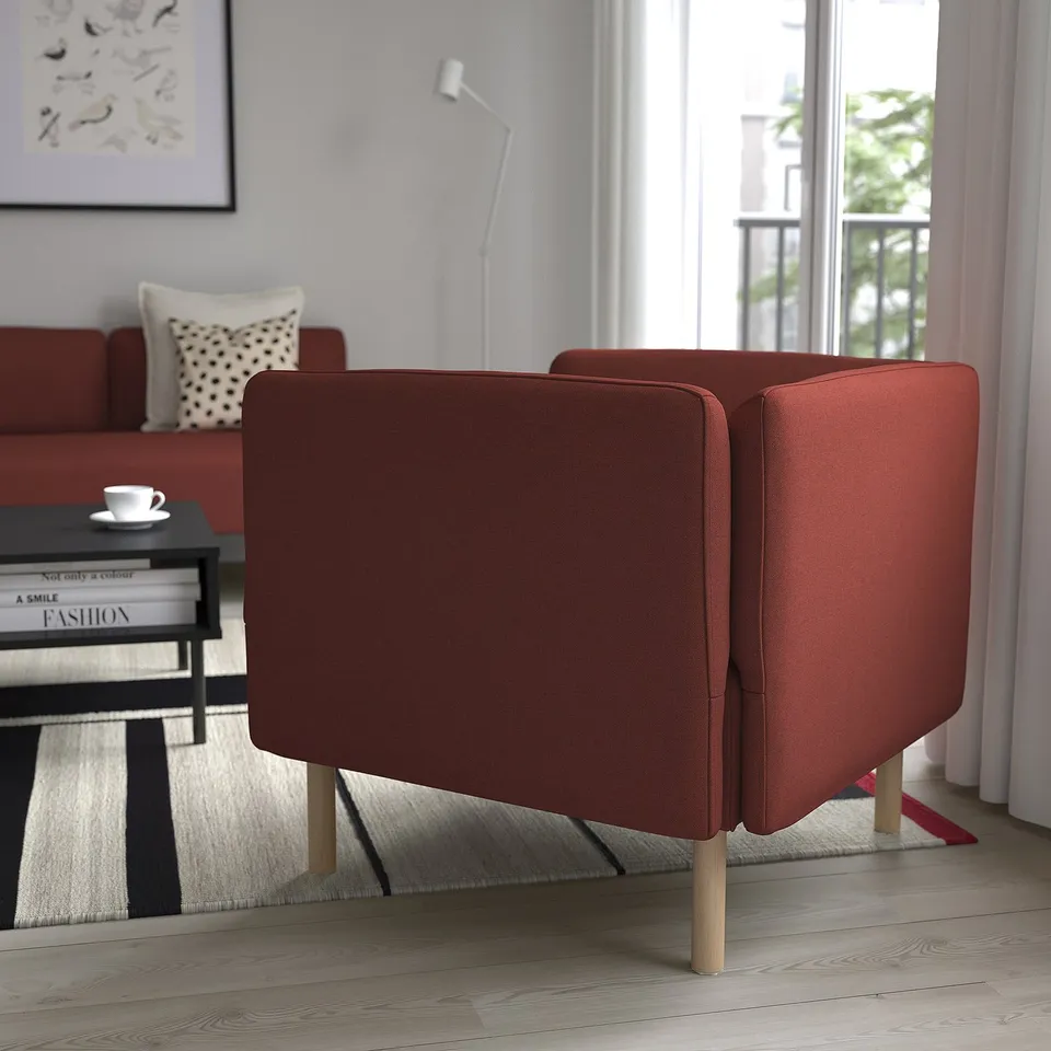 Bright living room with orange fabric armchairs, wooden floors, rug, coffee table with books, and large window.