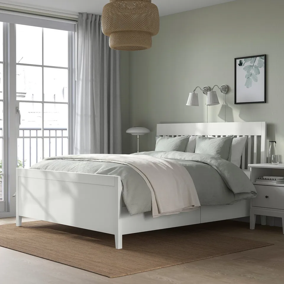 Bedroom with IDANÄS white bed, grey linens, large window, grey curtains, hanging lamp, bedside table with lamp, framed leafy artwork.