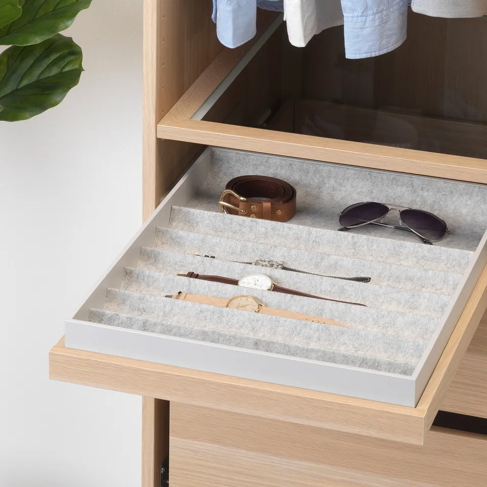 Drawer with KOMPLEMENT tray organising watches, belts, sunglasses, and more in a wardrobe.