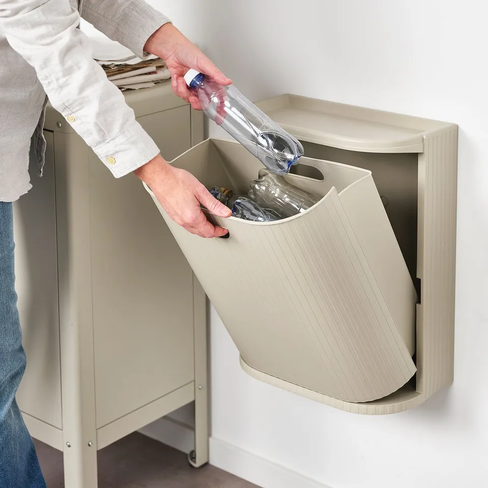 Person disposes empty water bottle into a wall-mounted, beige recycling bin, showcasing its accessibility and ease of use.