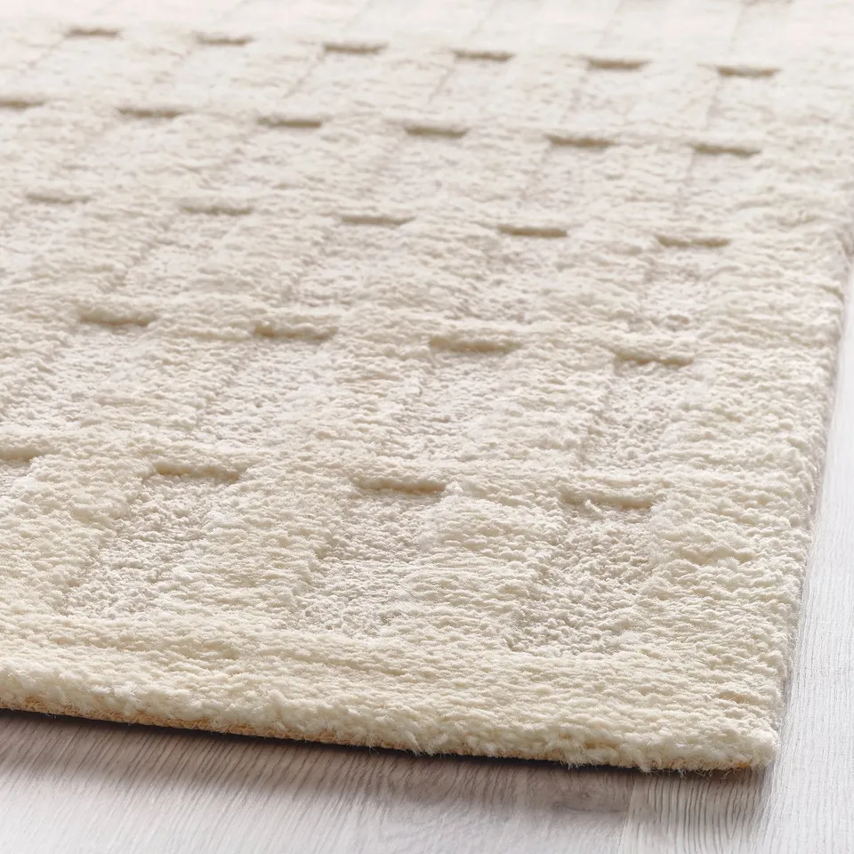 Close-up of a textured, off-white area rug with a looped pattern, placed on wooden flooring.