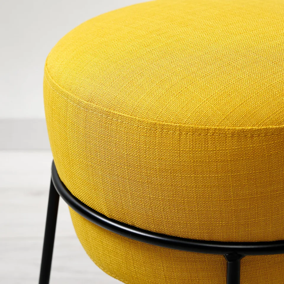 Bright yellow circular ottoman with black metal frame, showcasing high-quality fabric and sturdy construction.