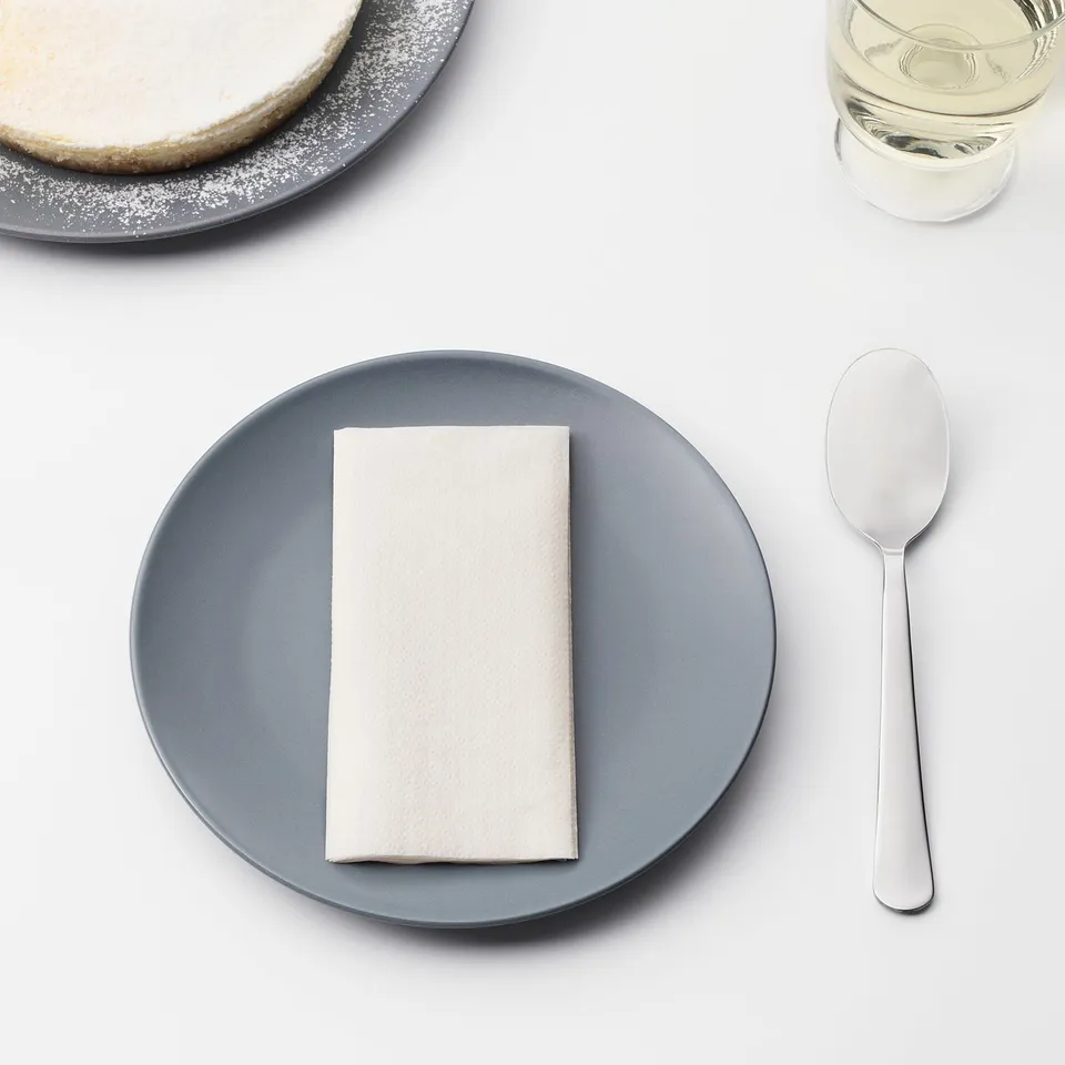A blue plate with folded white napkin and spoon, beside a cake on another plate and a glass of liquid.