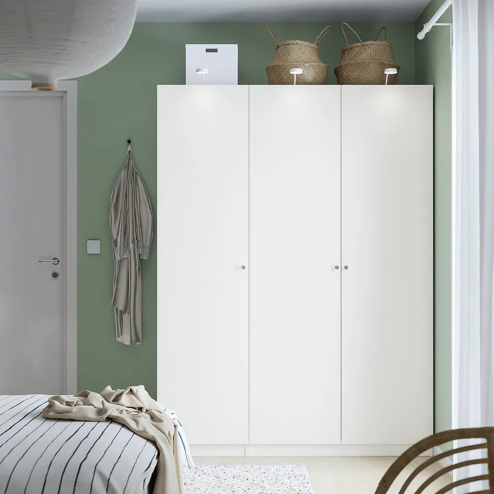 Minimalist bedroom with large white wardrobe, woven baskets, striped bed, and plush chair.
