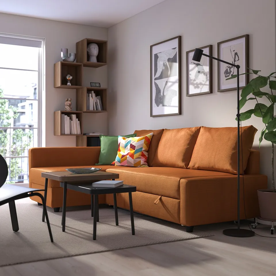 Bright orange FRIHETEN convertible sofa-bed, modern and cosy, fits well in the living room with a bookcase and plant.