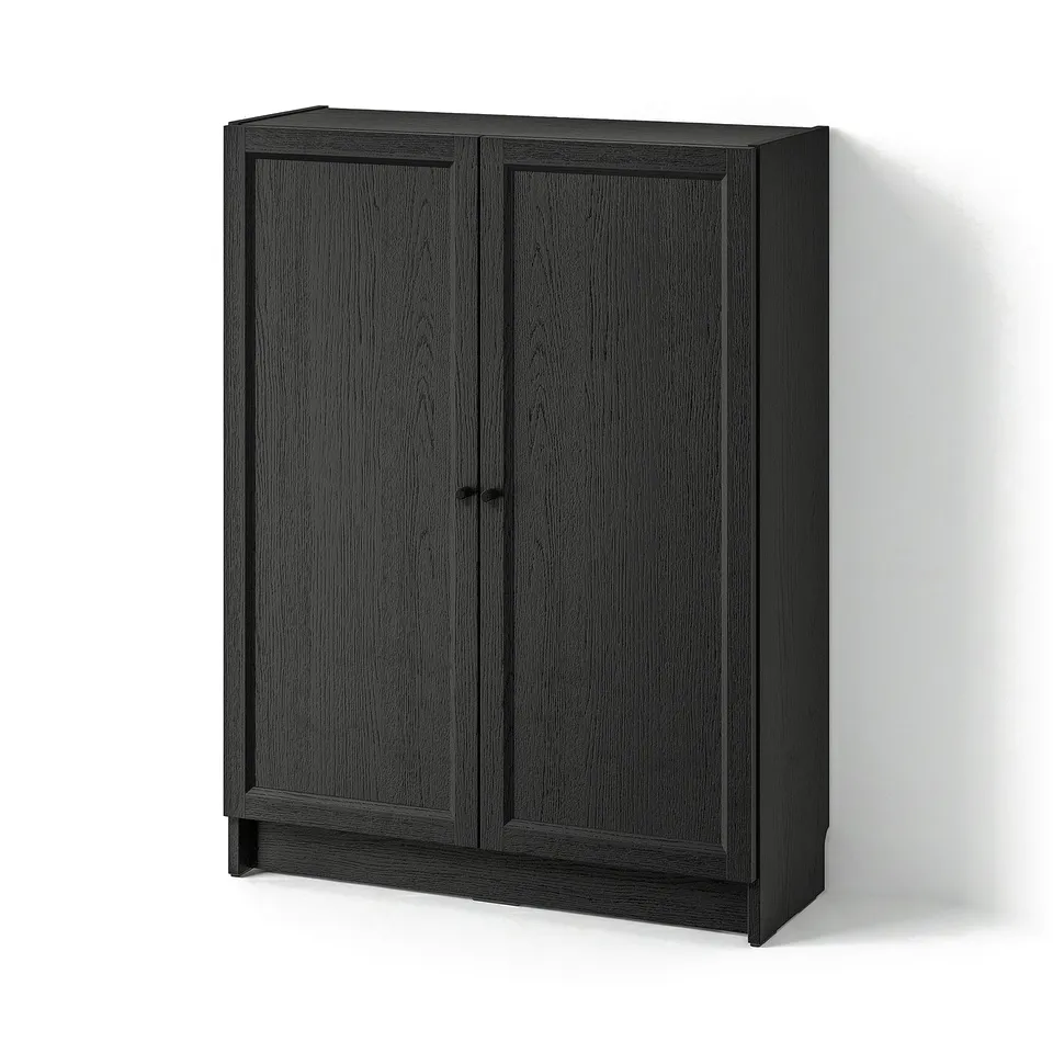 A BILLY bookcase in black. Its rectangular, has two doors with wooden panels, and stands against a wall.