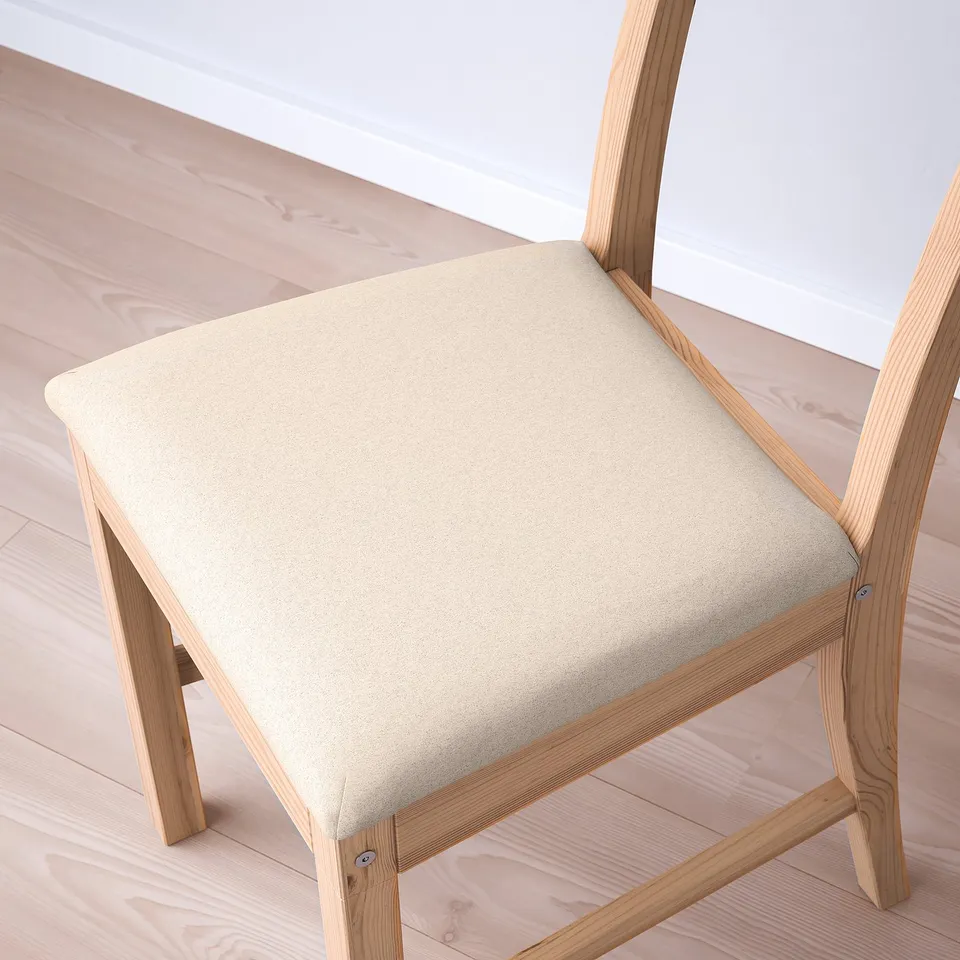 Modern angled wooden chair with soft, beige upholstered seat, set on light wood floor.