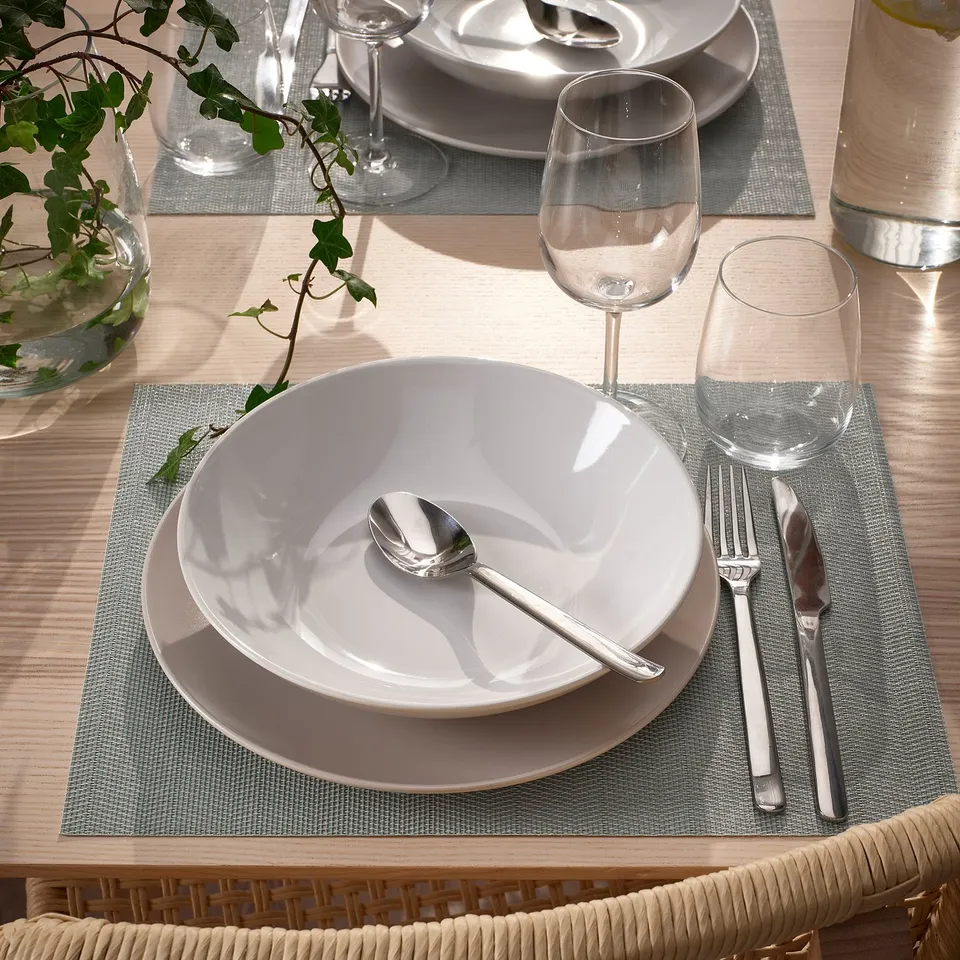 A table setting with FLYGFISK place mats, white plates, silverware, and wine glasses, creating an inviting atmosphere.
