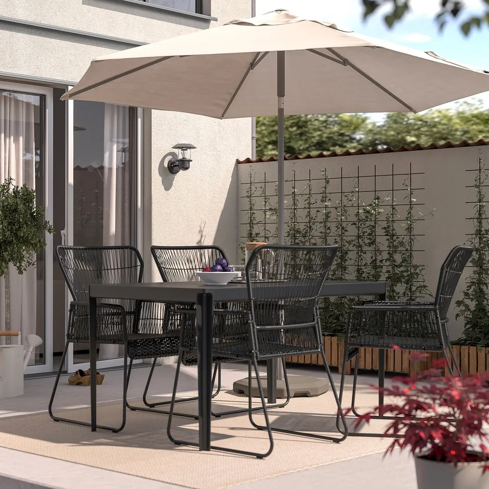 Modern patio with TALLSKÄR black chairs & beige umbrella, sleek design, ideal for dining or relaxing.