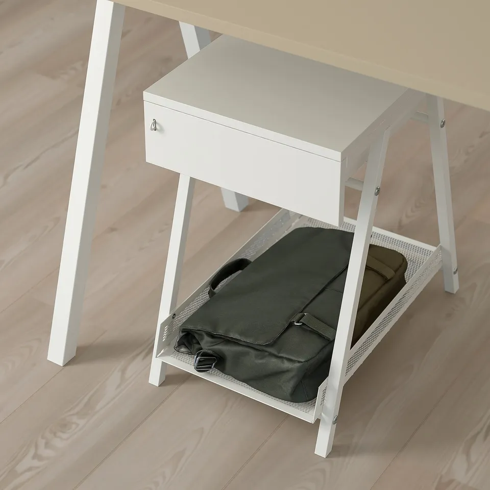 A small white desk with a drawer and a lower shelf. A black bag is stored on the shelf.