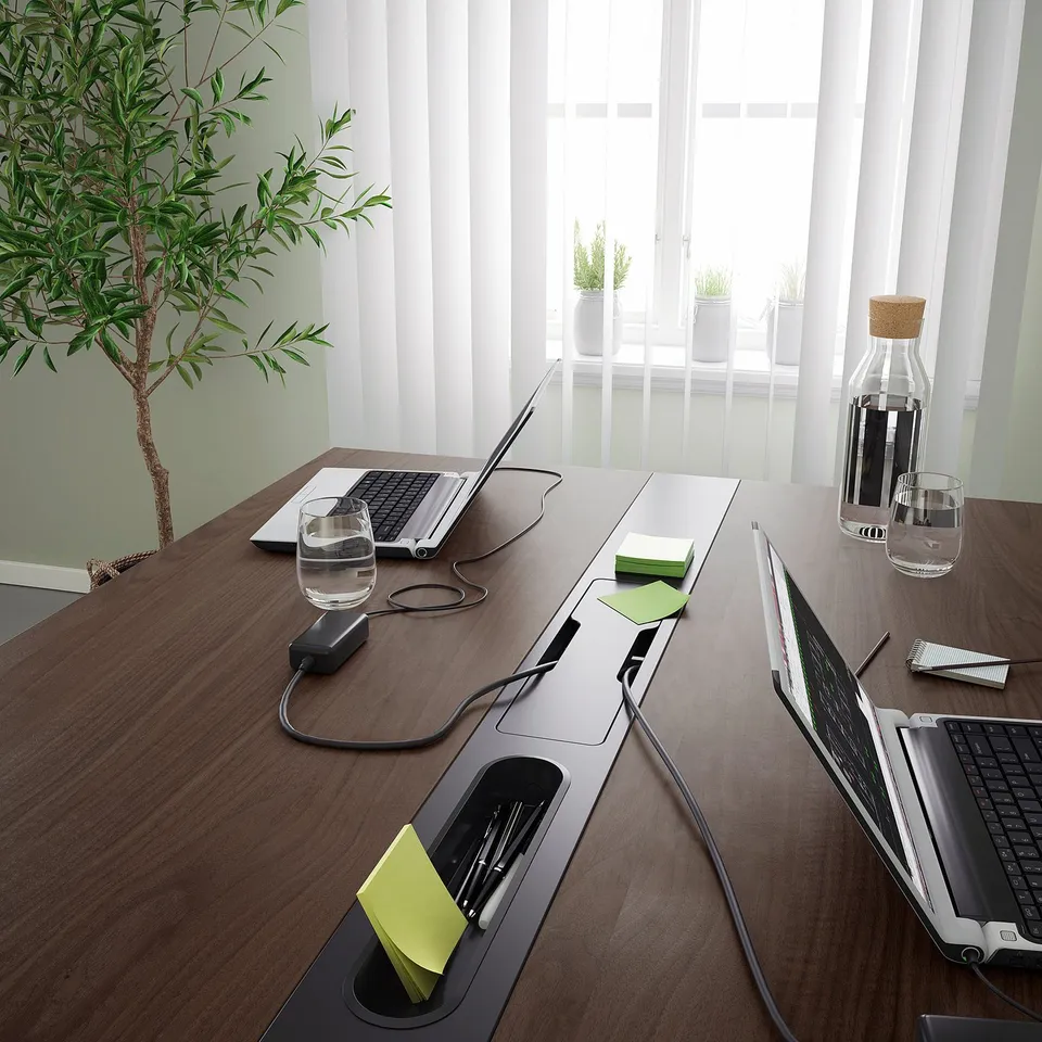 Modern conference table with power outlets, cable management, laptops, and a plant.