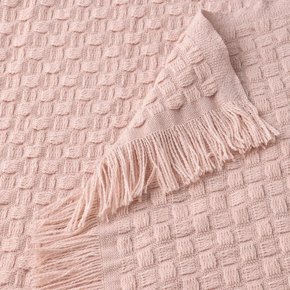 Light pink throw blanket with basket weave texture and fringes displayed, soft and cosy.
