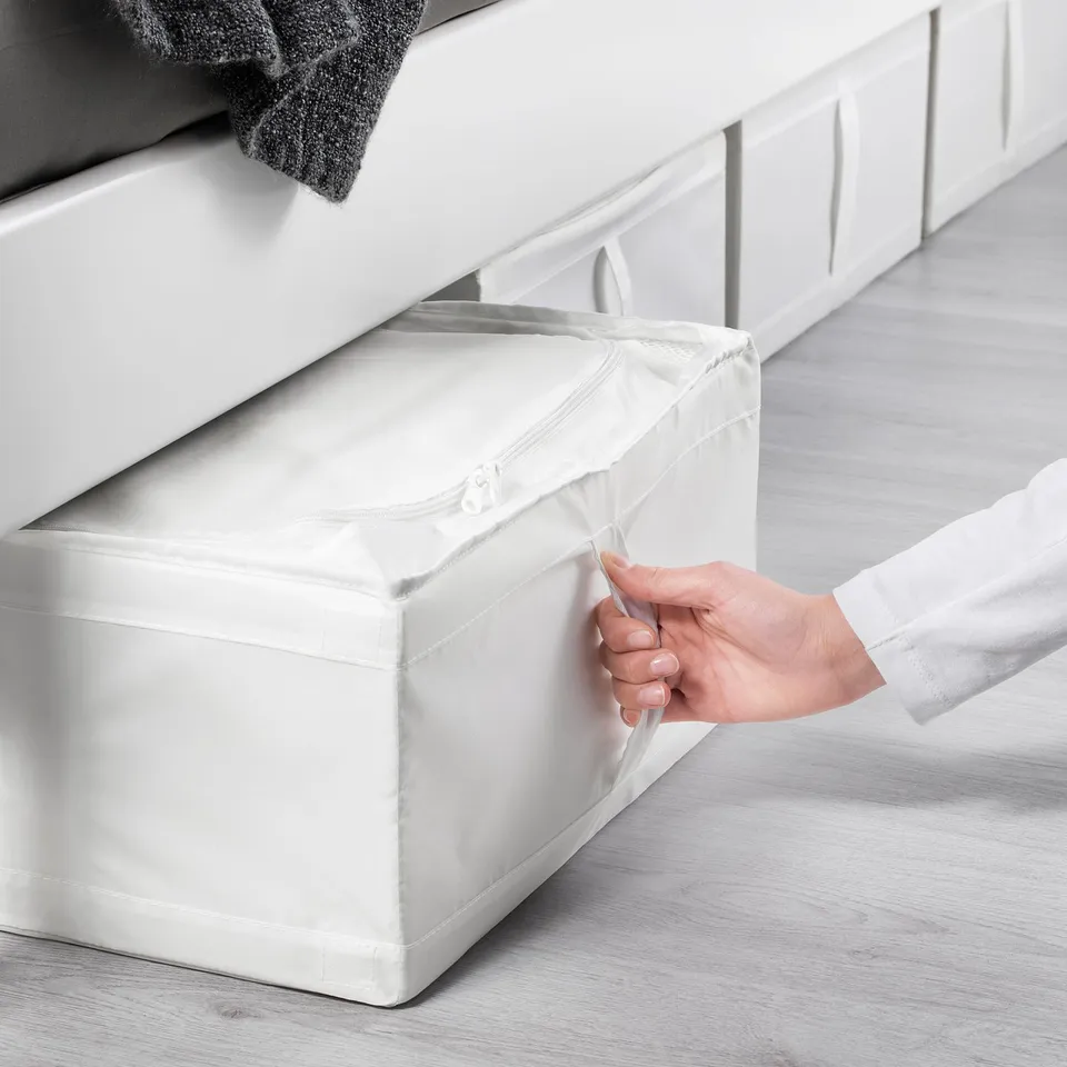 Hand opens white SKUBB storage under bed, keeping clothes dust-free.