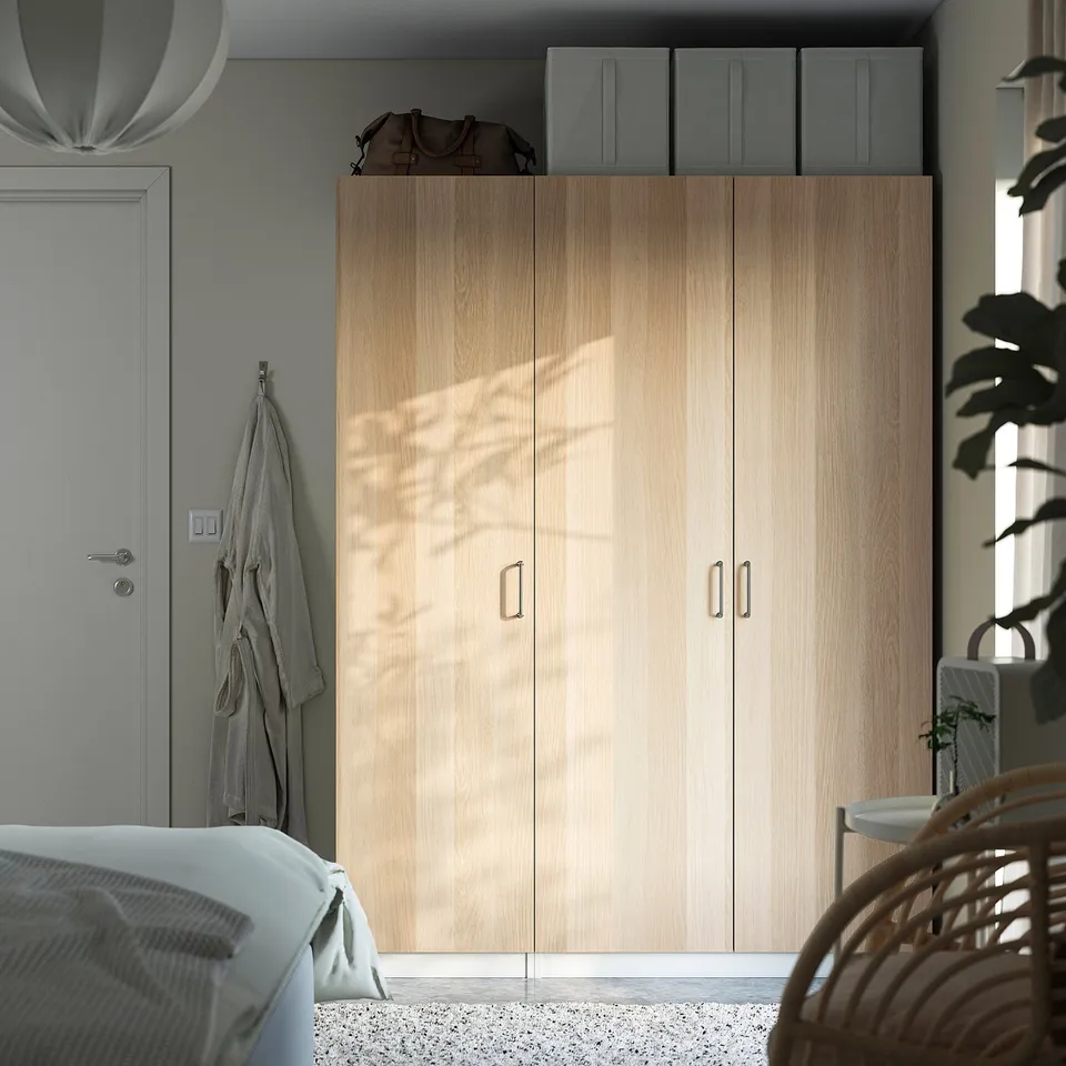 Modern bedroom with light wood PAX wardrobe, white door, blue boxes, robe, bed, chair, plant.