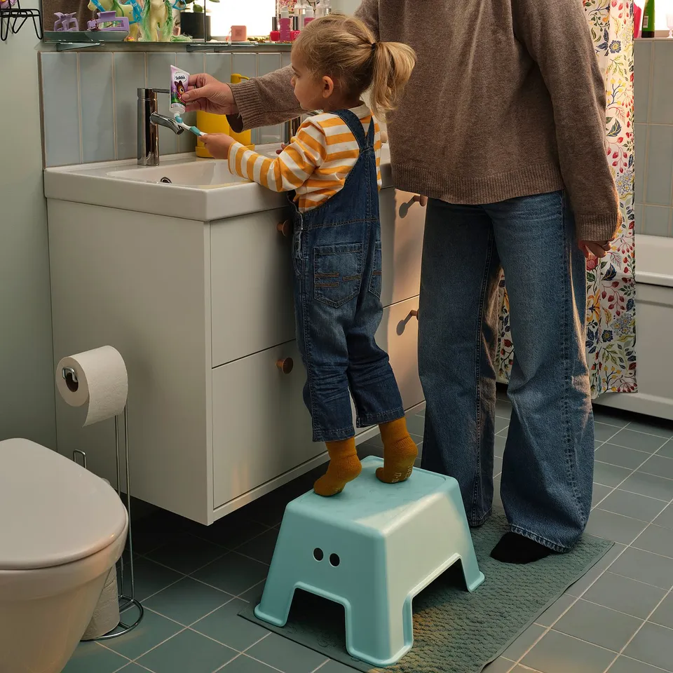Child on BOLMEN stool brushing teeth with adult.