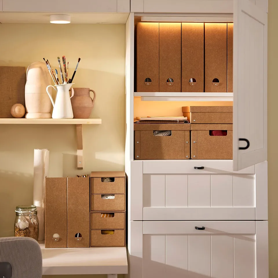 Office corner with GÄRDESGÅRD boxes organising papers. Tan recycled boxes stacked neatly. Open shelves display decor.