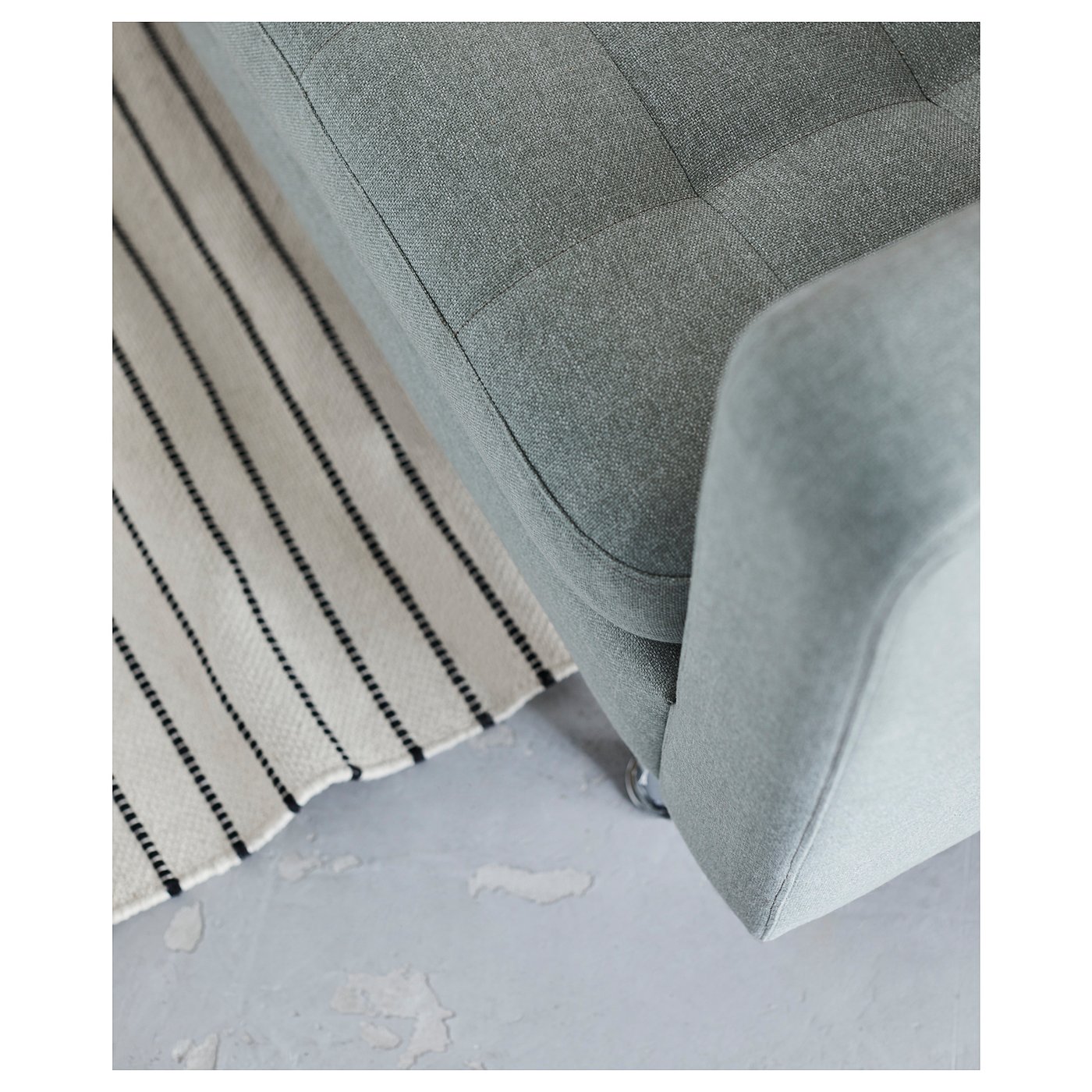 A corner of a grey landskröna armchair with a striped cushion.