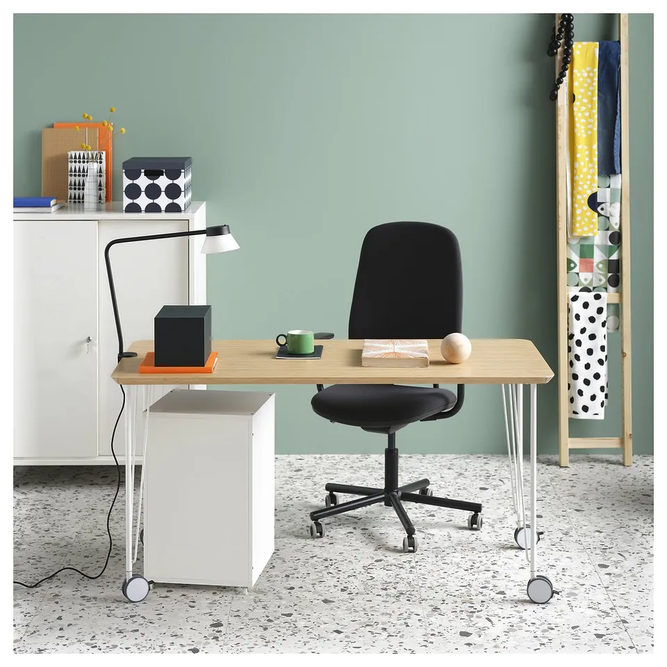 Home office with light wood desk, black chair, lamp, and green wall shelves.