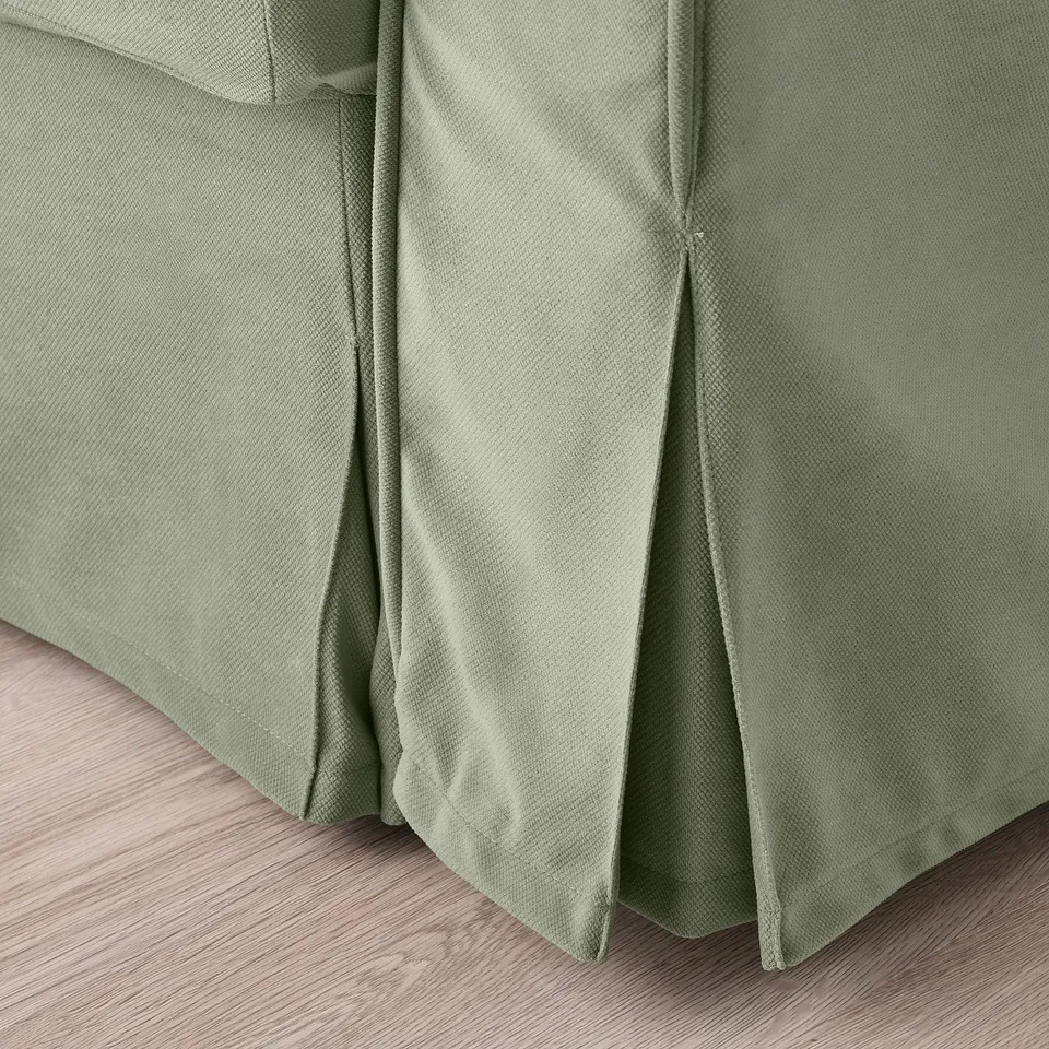 Sage green sofa-bed close-up, showcasing smooth, textured fabric and neatly tailored pleats.
