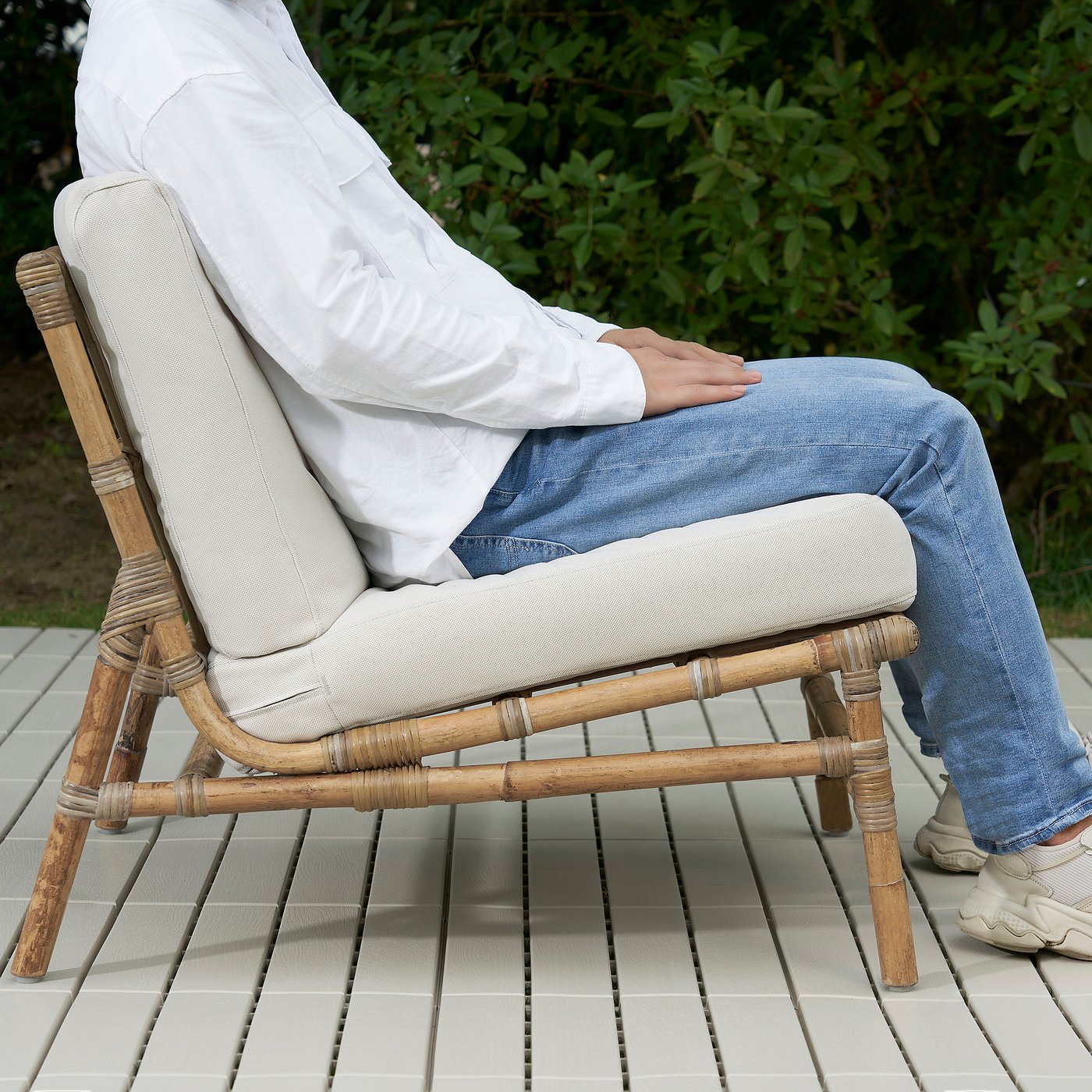 Person sitting on TVARÖ bamboo chair with cushion outdoors.