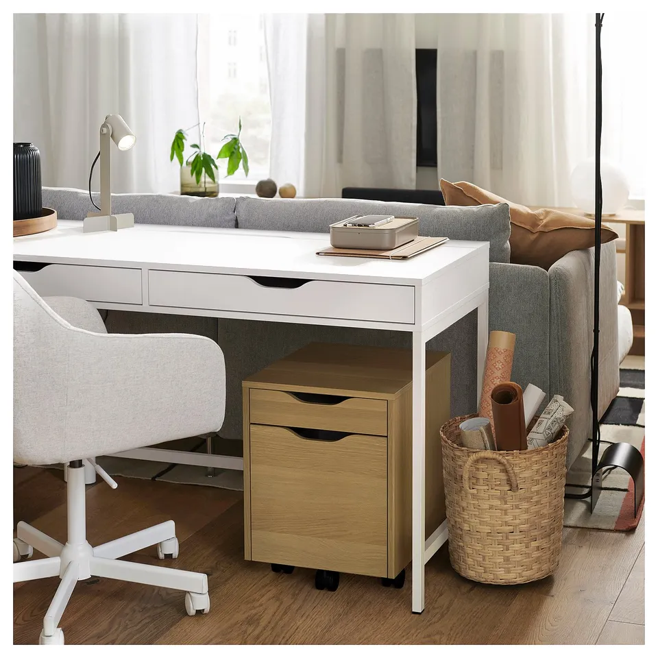 White ALEX desk with drawers and basket, laptop on tray, near sofa in bright room.