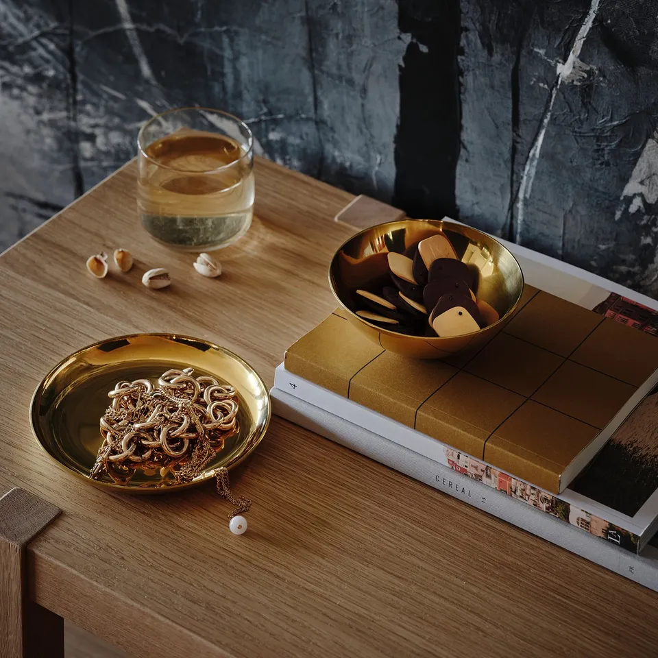 Bowl and dish set on table, holding jewellery and small items, with drink and book.