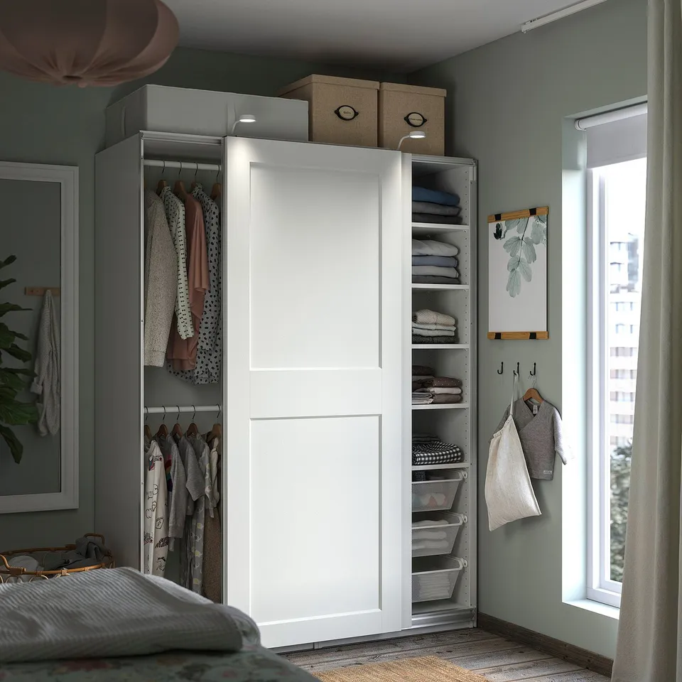 Neat bedroom with white PAX wardrobe, clothes, and shelves. Green walls, with natural light from window and curtains.