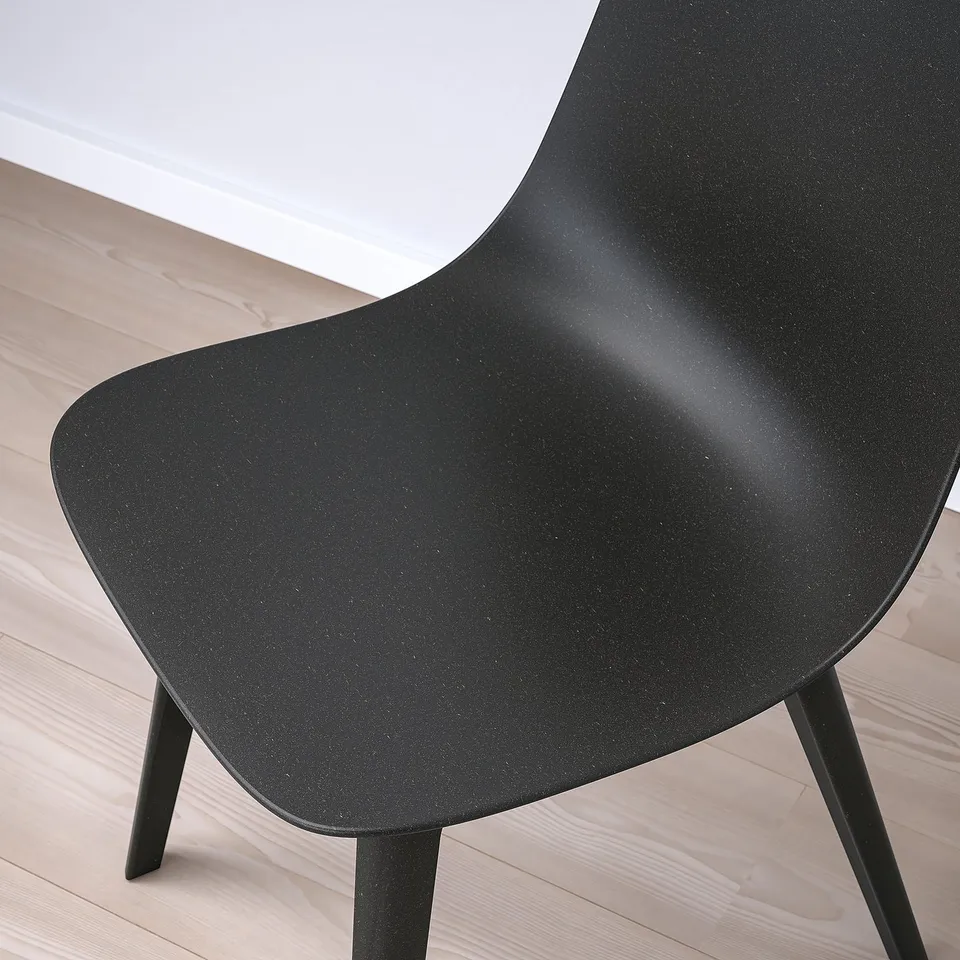 Black modern chair with sleek curves and dark legs, positioned on a light wooden floor.