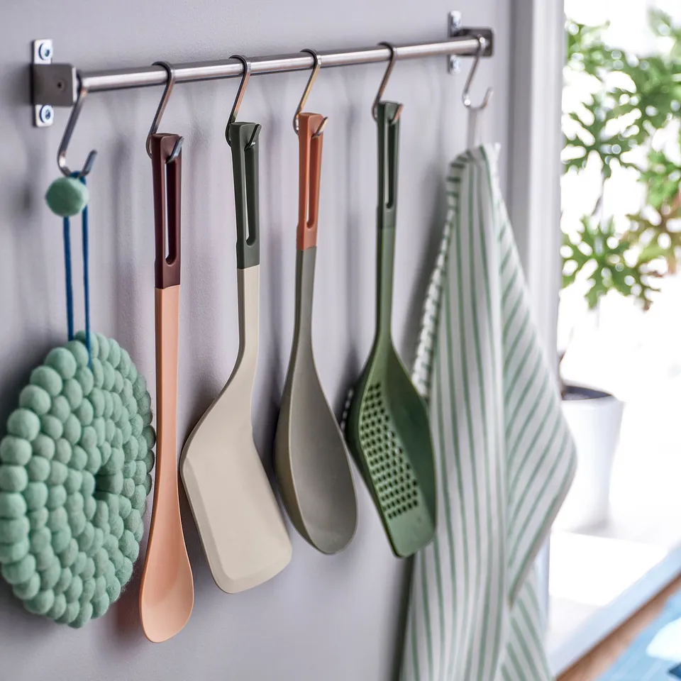 Colourful kitchen utensils hang from hooks. Includes spatulas and straining spoon, easy to hang and use.