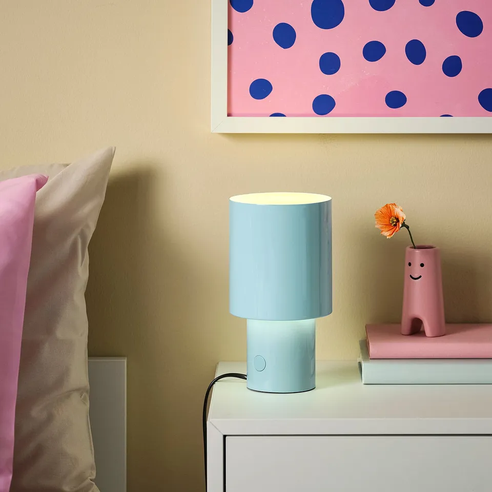 SPETSBOJ lamp in bedroom, light blue, on white dresser with pink book and orange flower.