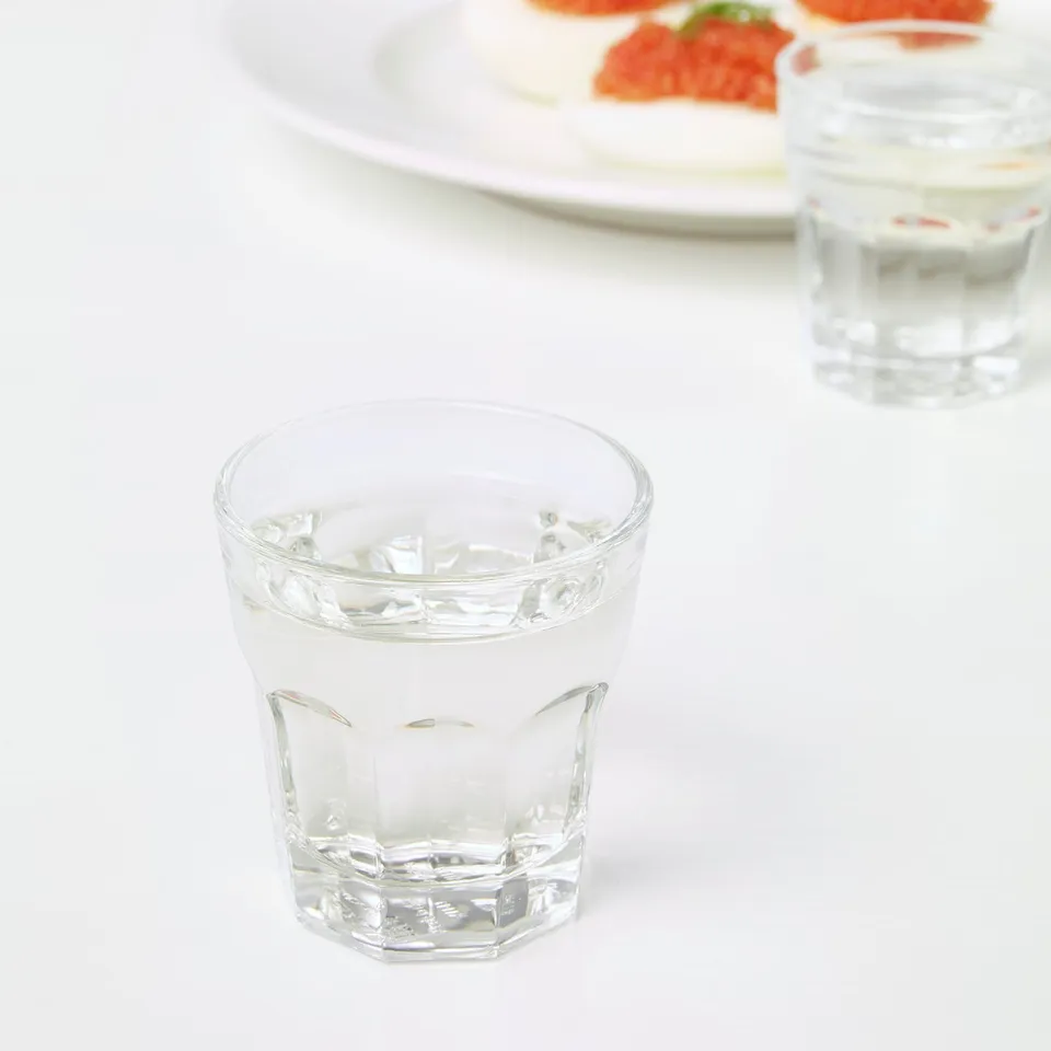 Two glasses with ice sit on a white table, beside a plate with food.