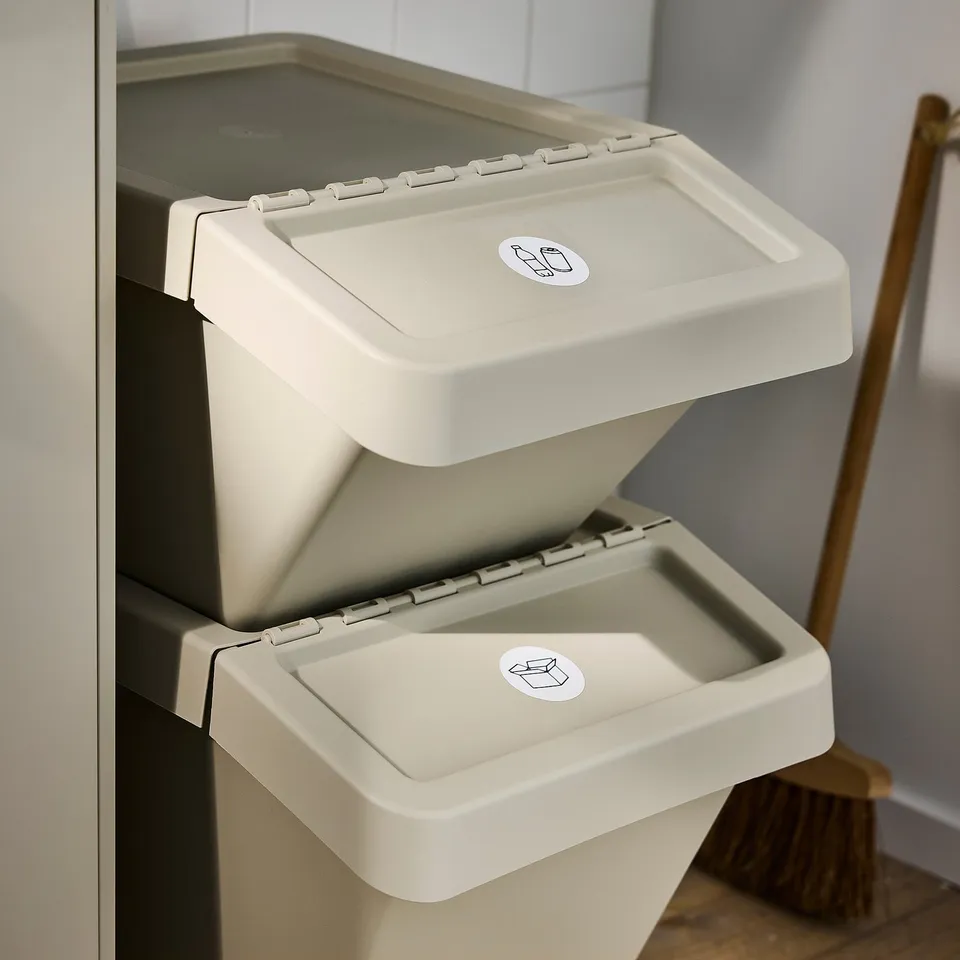 Stacked SORTERA waste bins with foldable lids, ideal for sorting different types of waste. Lids have stickers showing recycling symbols.
