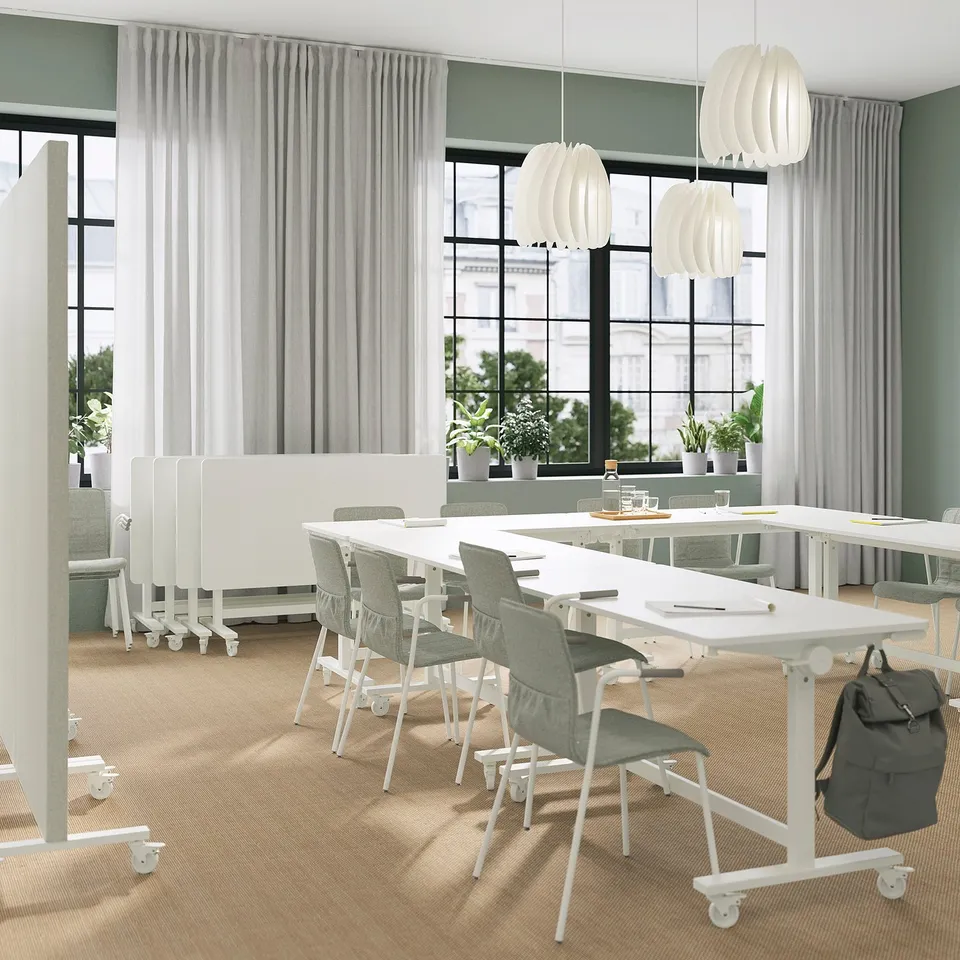 Modern meeting space with MITTZON tables; white, rectangular, on wheels. Chairs, potted plants, and large windows.