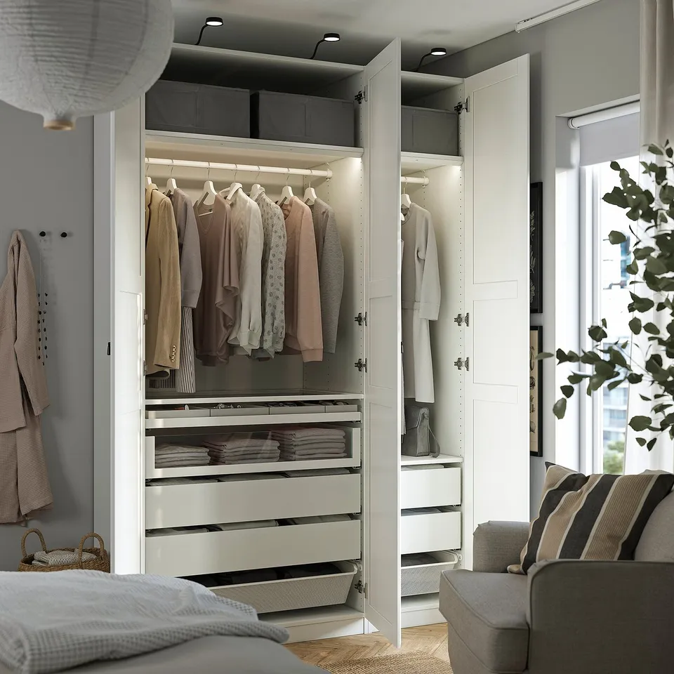 Open wardrobe with clothes, drawers, and lighting.