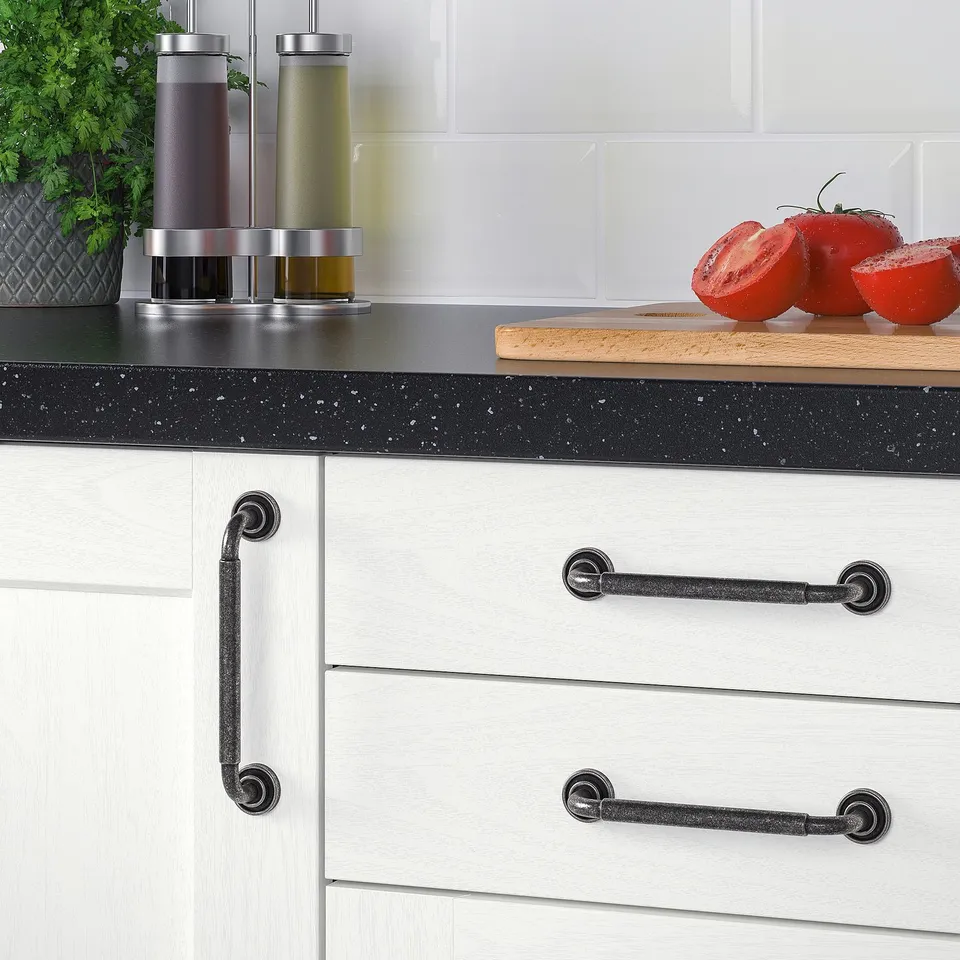 Kitchen cabinets with anthracite handles. Two large red tomatoes on a wooden board, three spice dispensers, and a green plant beside.