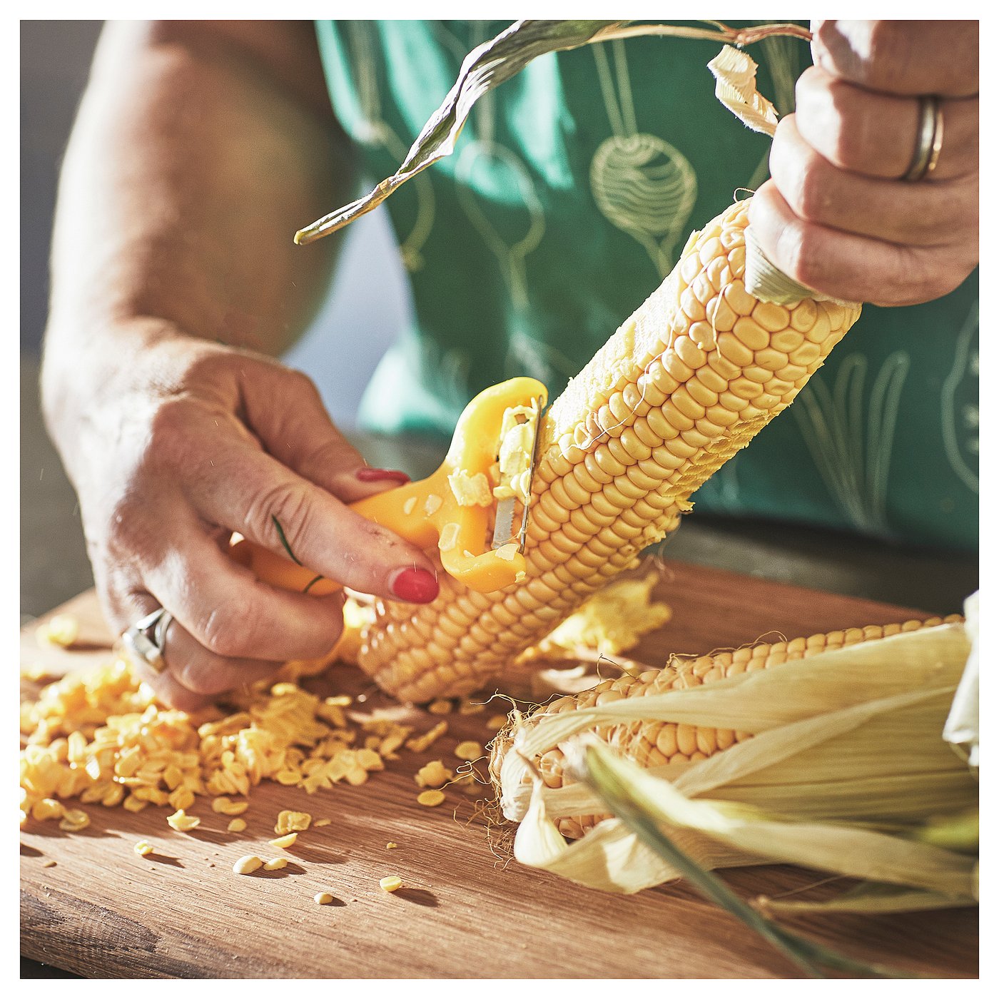 Person uses yellow UPPFYLLD peeler on corn; kernels scattered.