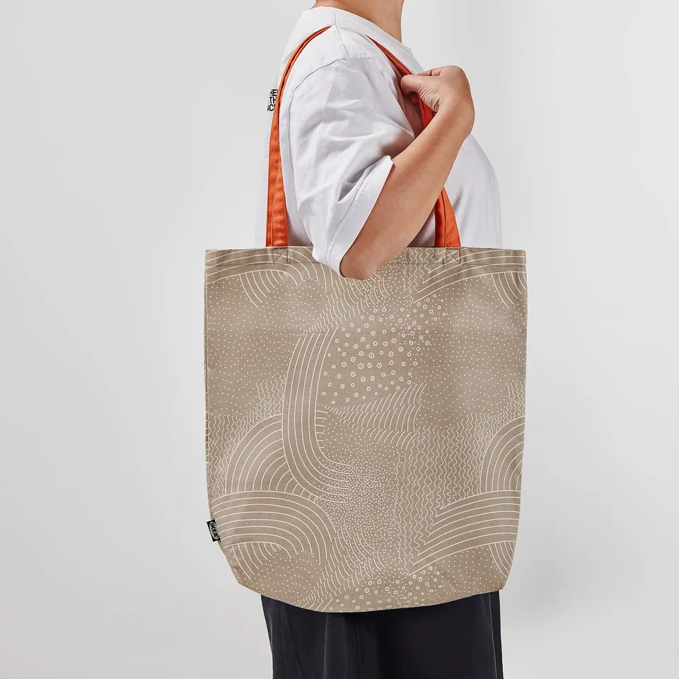 Person holding large beige tote bag with orange handles and white circular patterns.