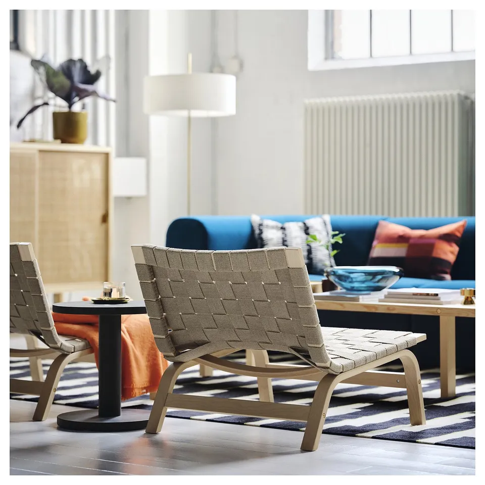 A modern scandinavian-style easy chair with a woven linen band seat and bent birch frame in a minimalist living room.