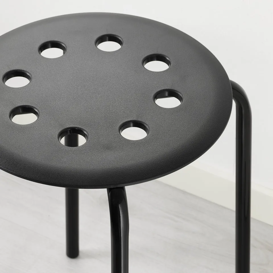 Black modern stool with round seat and metal legs, designed for stacking, shown on light-colored floor.