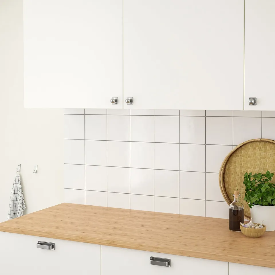 Modern kitchen counter with white cabinets, bamboo veneer top, green plant, wooden tray, and towel hook.